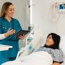 Doctor with clipboard talking to patient in hospital bed