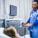 Healthcare worker at computer talking to patient in hospital bed