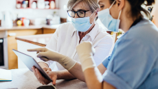 Healthcare worker with mask pointing to tablet held by woman in mask.