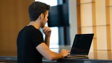 Man in black tshirt codes on a laptop