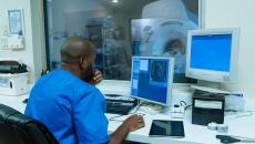 Healthcare worker looking at computer screen with MRI room in background