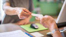 Person behind a desk handing a slip of paper to another