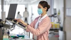 A nurse checking a patient's file on a laptop in the hospital corridor