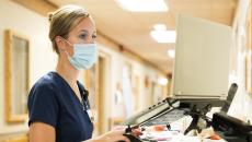 A nurse checking a patient's record on a hallway laptop