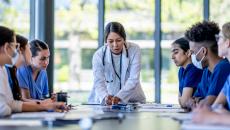 Doctor pointing out item on table to group of sitting healthcare workers