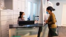 Patient in mask talking to receptionist in mask