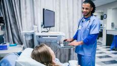 Healthcare worker at computer talking to patient in hospital bed