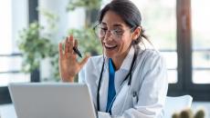 Doctor with glasses seated speaks during a telehealth visit via laptop