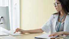 A doctor looking over a patient file on a desktop computer