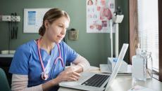 Healthcare provider in blue scrubs sitting at a desk looking at a computer