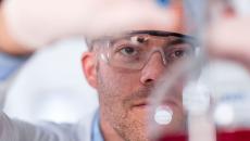 Lab worker with safety glasses looking into a beaker