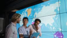 Workers looking at a tablet with world map projected in background