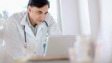 Male doctor leans over a laptop on a counter