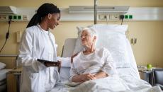 A doctor holding a digital tablet interacting with a senior patient in bed.