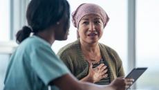 Patient with kerchief speaks to a clinician and reviews information on a tablet.