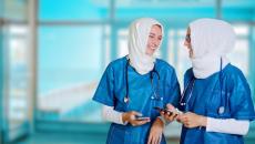 Nurses wearing hijabs conversing while holding their smartphones