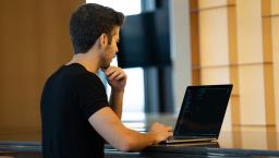 Man in black tshirt codes on a laptop