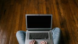 Laptop on a mans lap sitting on an oak wood floor