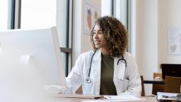 A doctor reviewing a patient's file on a desktop computer