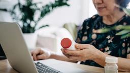 Person sits at table with a laptop while holding a pill bottle