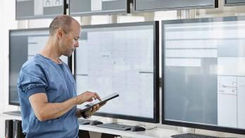 Healthcare worker with tablet looking at data displays