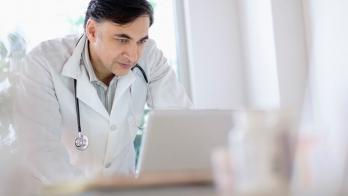 Male doctor leaning over a laptop