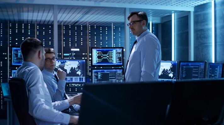 Three cybersecurity professionals talk in a network control room.