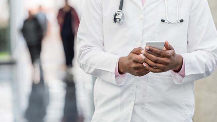 A doctor in a lab coat standing and texting in a hallway 