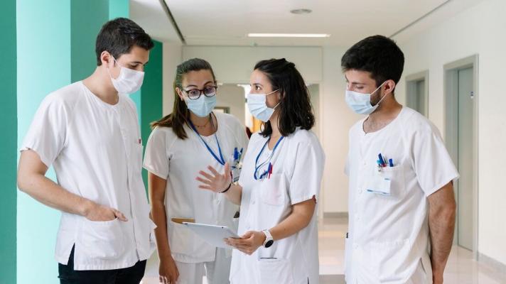 One healthcare worker talks with colleagues and references data on a tablet.